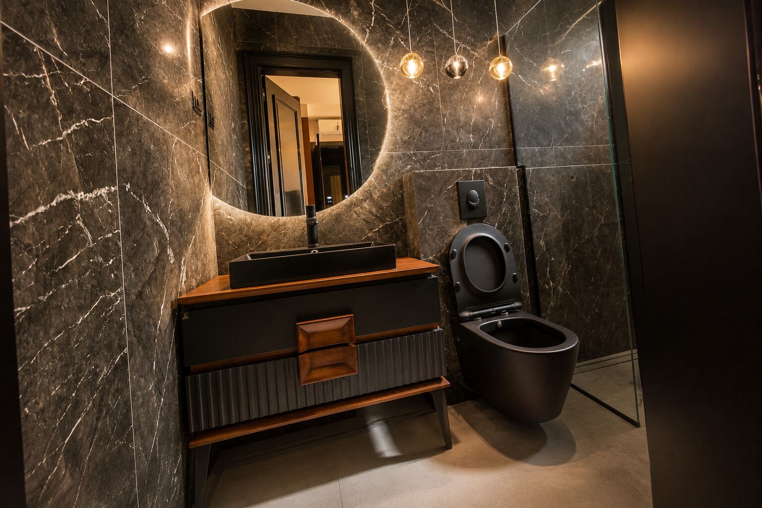 Un baño moderno con pared de mármol, tocador de madera, inodoro negro y espejo redondo con iluminación colgante.