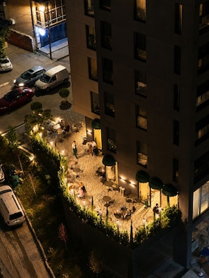Un espacio exterior para comer con mesas y sillas, rodeado de vegetación e iluminado con luces ambientales.