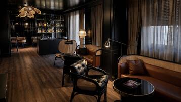 A dimly lit lounge area with leather sofas, a bar area with bottles, and a bookshelf.