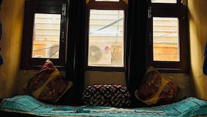 A room with a bench, three windows, and a patterned cushion.