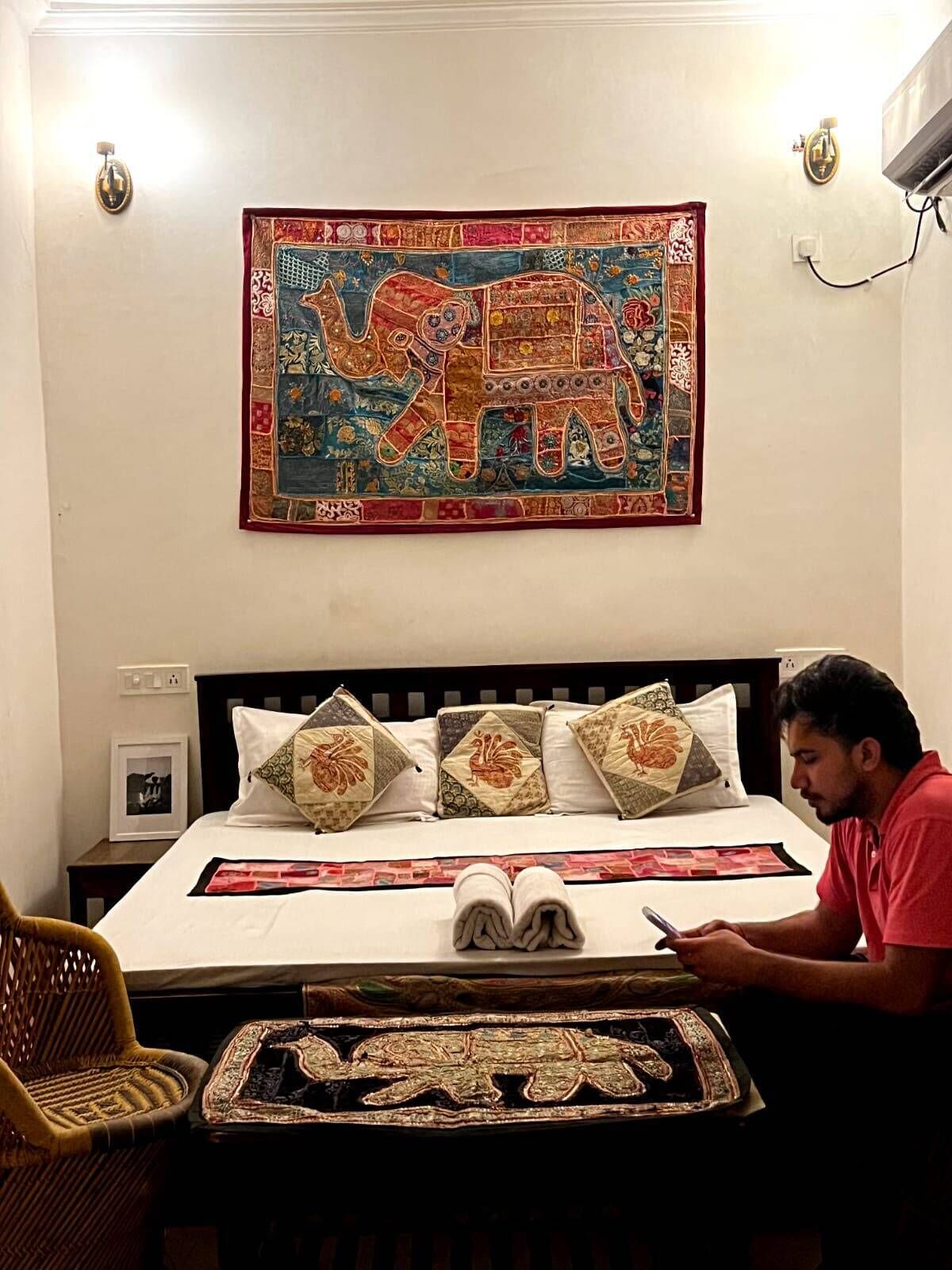 A room with a bed, a wall tapestry, a chair, and a table with a decorative item.