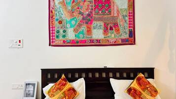 A bed with two pillows, a nightstand with a framed photo, and a colorful tapestry on the wall.