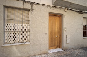 A building with a wooden door, a window with a metal grid, and a number '61' on the wall.