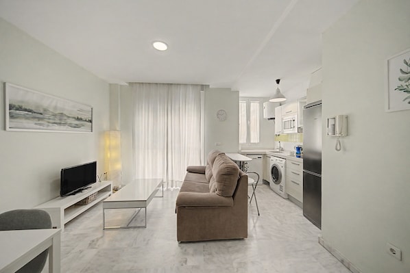 A modern living room with a sofa, a flat-screen TV, and a dining table.