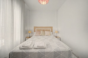 A hotel room with a large bed, two bedside lamps, and sheer curtains.