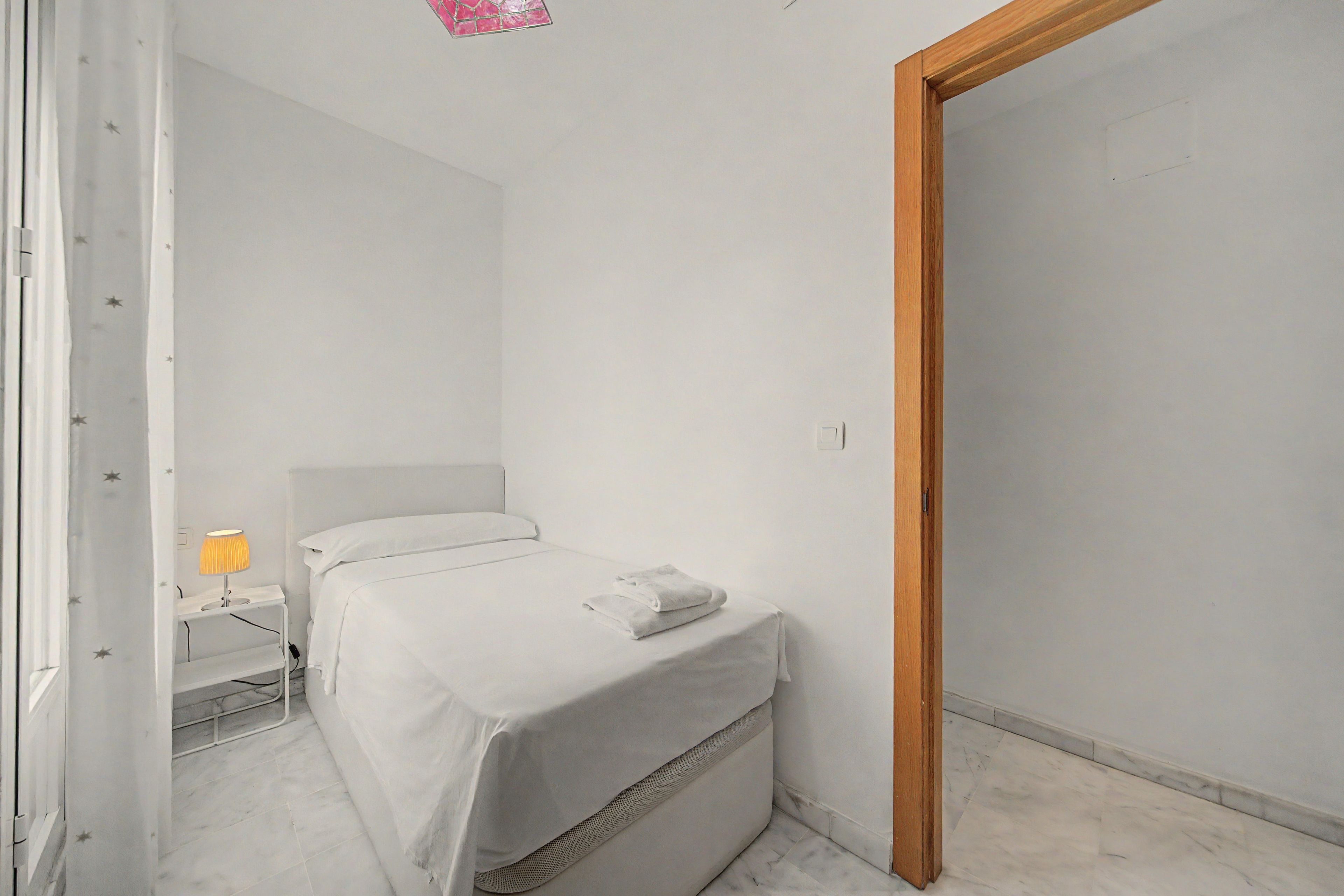Une chambre à coucher minimaliste avec un lit simple, une table de chevet avec une lampe et une porte en bois.