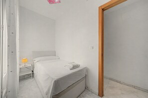 Ein schlicht eingerichtetes Schlafzimmer mit einem Einzelbett, einem Nachttisch mit Lampe und einer Holztür.