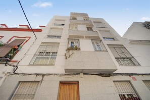 Un immeuble à plusieurs étages doté d’une façade plane, de plusieurs fenêtres avec des barreaux en métal et d’une porte en bois au niveau du rez-de-chaussée.
