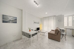 A modern living room with a sofa, a dining table with chairs, a television, and artwork on the walls.