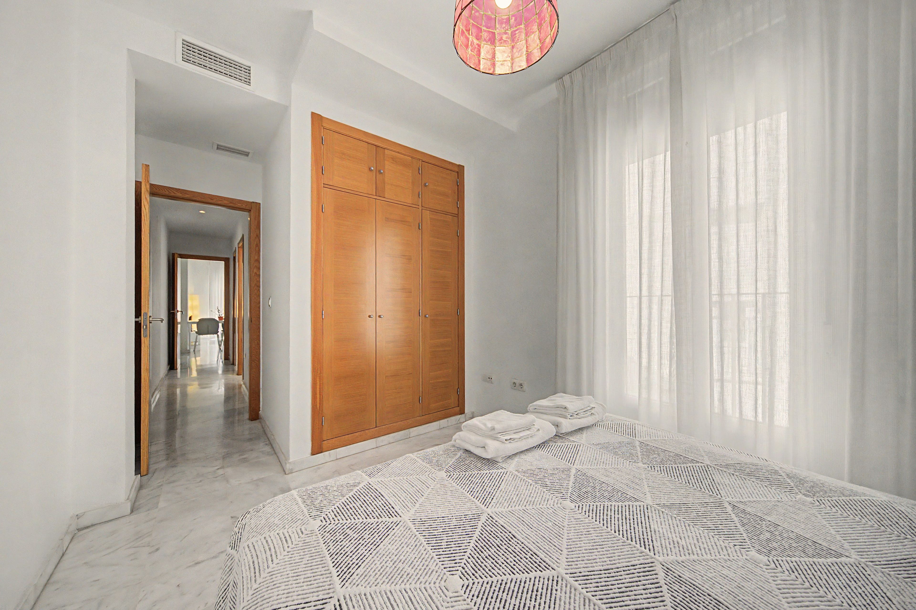 Une chambre avec une grande armoire, un lit recouvert d’une couvre-lit à motifs et donnant sur un couloir.