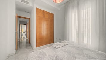 Une chambre avec une grande armoire, un lit recouvert d’une couvre-lit à motifs et donnant sur un couloir.
