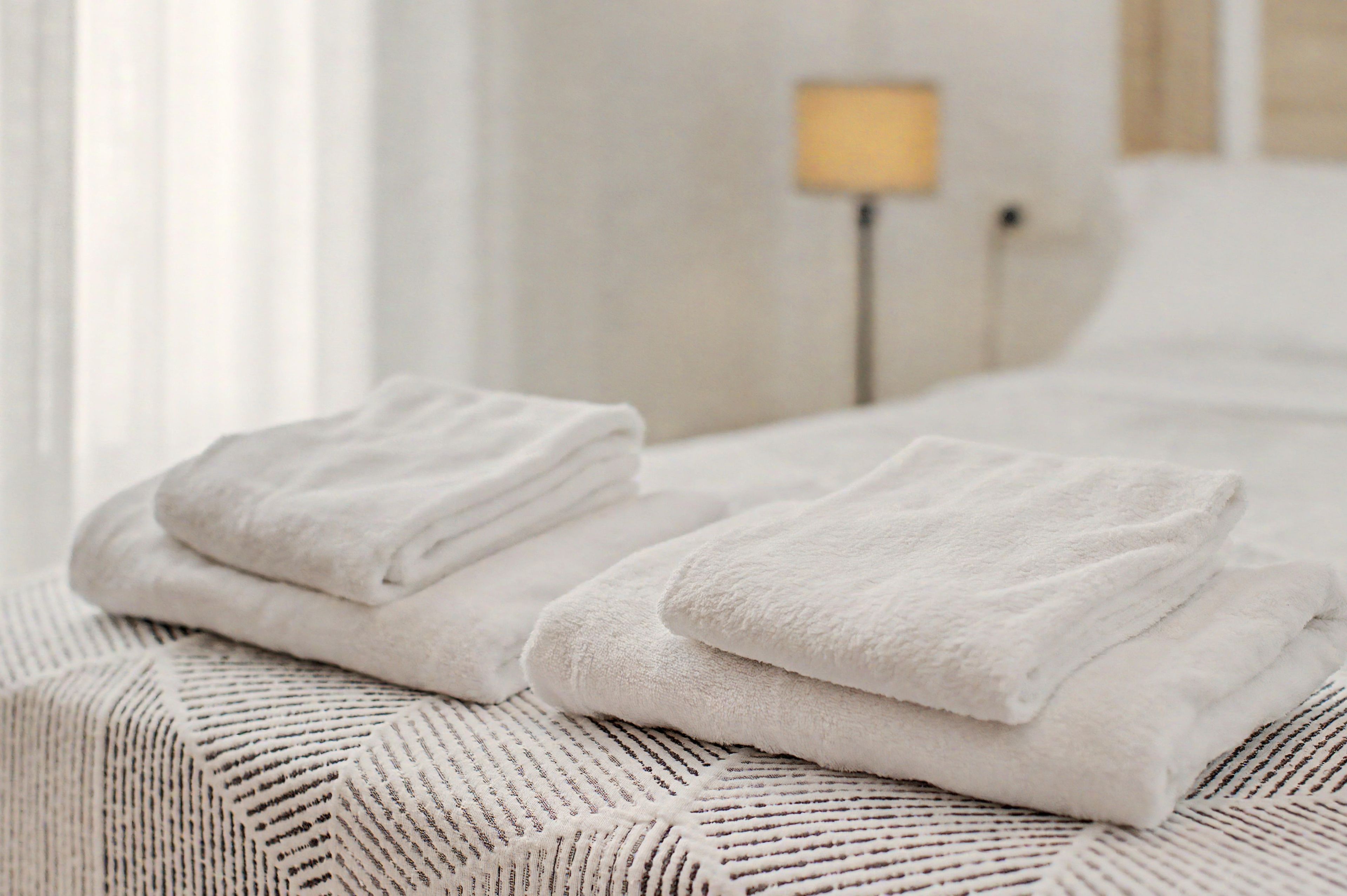 Una cama bien hecha con toallas blancas dobladas y una manta decorativa.