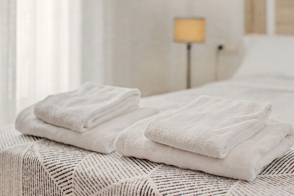 A neatly made bed with folded white towels and a patterned throw blanket.
