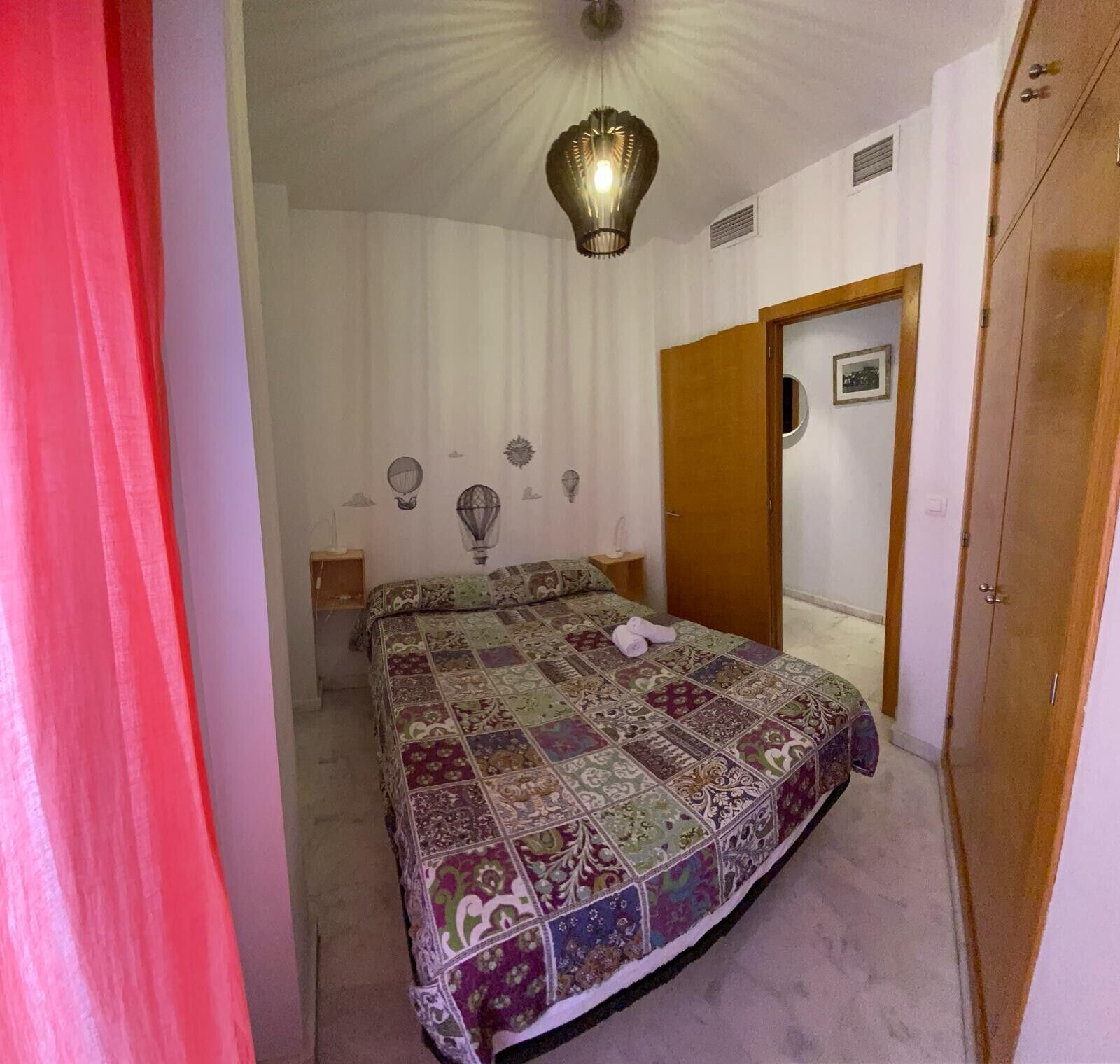 Une chambre à coucher avec un lit, une table de chevet, une lampe fixée au mur et une porte.
