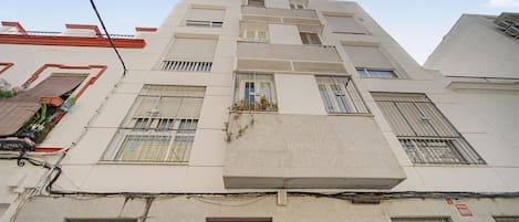 Un edificio de varios pisos con fachada plana, varias ventanas con rejas de metal y una puerta de madera al nivel de la calle.