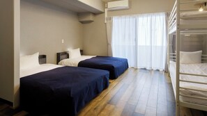 Habitación de hotel con dos camas, una litera, suelo de madera, una ventana con cortinas translúcidas y un equipo de aire acondicionado.