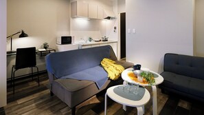 Un espacio habitable compacto con un sofá, una mesa de comedor con sillas, una kitchenette y una pequeña mesita con una planta.