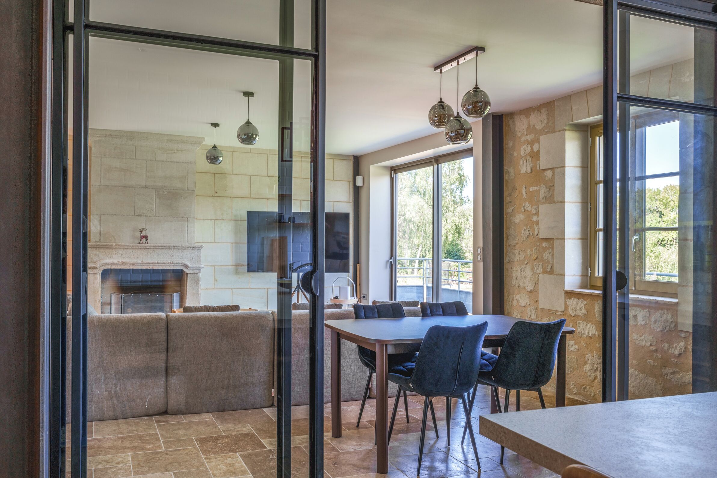 A modern kitchen with a fireplace, a dining area with a table and chairs, and large windows.