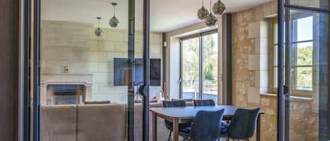 A modern kitchen with a fireplace, a dining area with a table and chairs, and large windows.