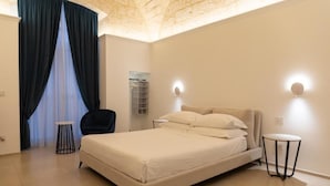 A bedroom with a bed, a chair, a small table, and a wall-mounted shelf. - Mas Collection - Dimora Zonno (Bari)