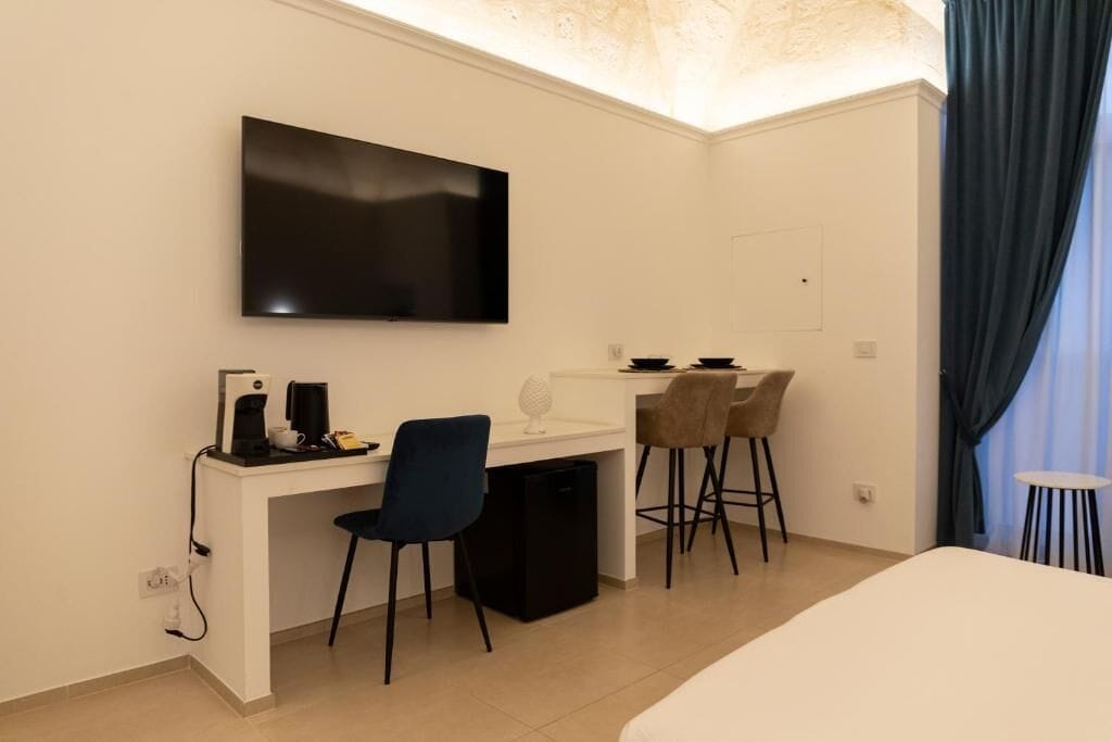 A hotel room with a bed, a desk with a chair, a television, and a small table with a chair.