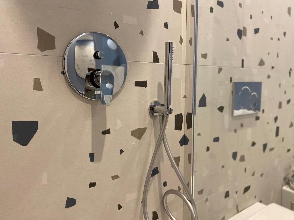 Un baño con ducha, espejo y pared con diseño de baldosas geométricas.