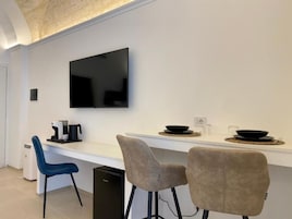 Una cocina moderna con un televisor de pantalla plana montado en la pared, una encimera blanca y dos taburetes de bar.