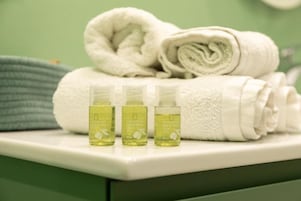 Un baño con una toalla blanca, una toalla verde y tres botellas de loción sobre un mostrador blanco.
