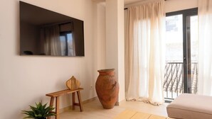 A living room with a flat-screen TV, a potted plant, a wooden stool, a large vase, a sofa, and a sliding glass door leading to a balcony. - Estepona Old Town (200 meters from the beach) (Estepona)