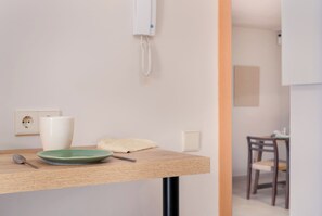 Ein Zimmer mit einem Holztisch, einem grünen Teller, einer weißen Vase, einem weißen Telefon und einem Holzstuhl.