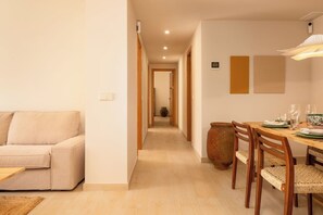 Ein modernes Wohnzimmer mit einer Couch, einer Essecke mit Tisch für zwei Personen und einem Flur, der in ein weiteres Zimmer führt.