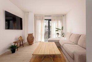 Un salon moderne avec un canapé, une table basse en bois, une plante en pot, un grand vase et un téléviseur à écran plat fixé au mur.