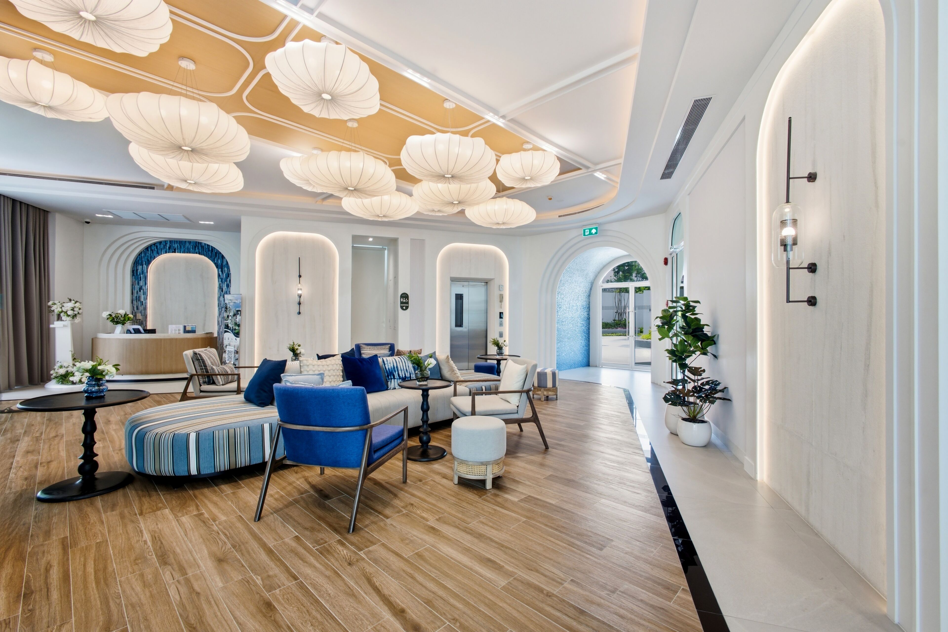 A modern hotel lobby with a wooden floor, seating area with sofas and chairs, and a reception desk.