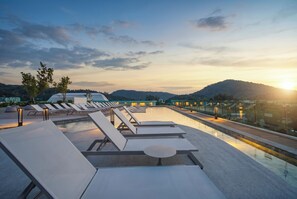 A rooftop pool area with lounge chairs and a view of the sunset over hills. - Cozy 1-bedroom apartment in Title Serenity Naiyang (Thalang District)