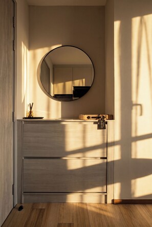 A modern bathroom with a wooden vanity, a round mirror, and a small sink. - Cozy 1-bedroom apartment in Title Serenity Naiyang (Thalang District)