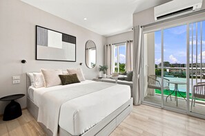 A modern bedroom with a large bed, a bedside table, a mirror, and a view of a swimming pool. - Cozy 1-bedroom apartment in Title Serenity Naiyang (Thalang District)