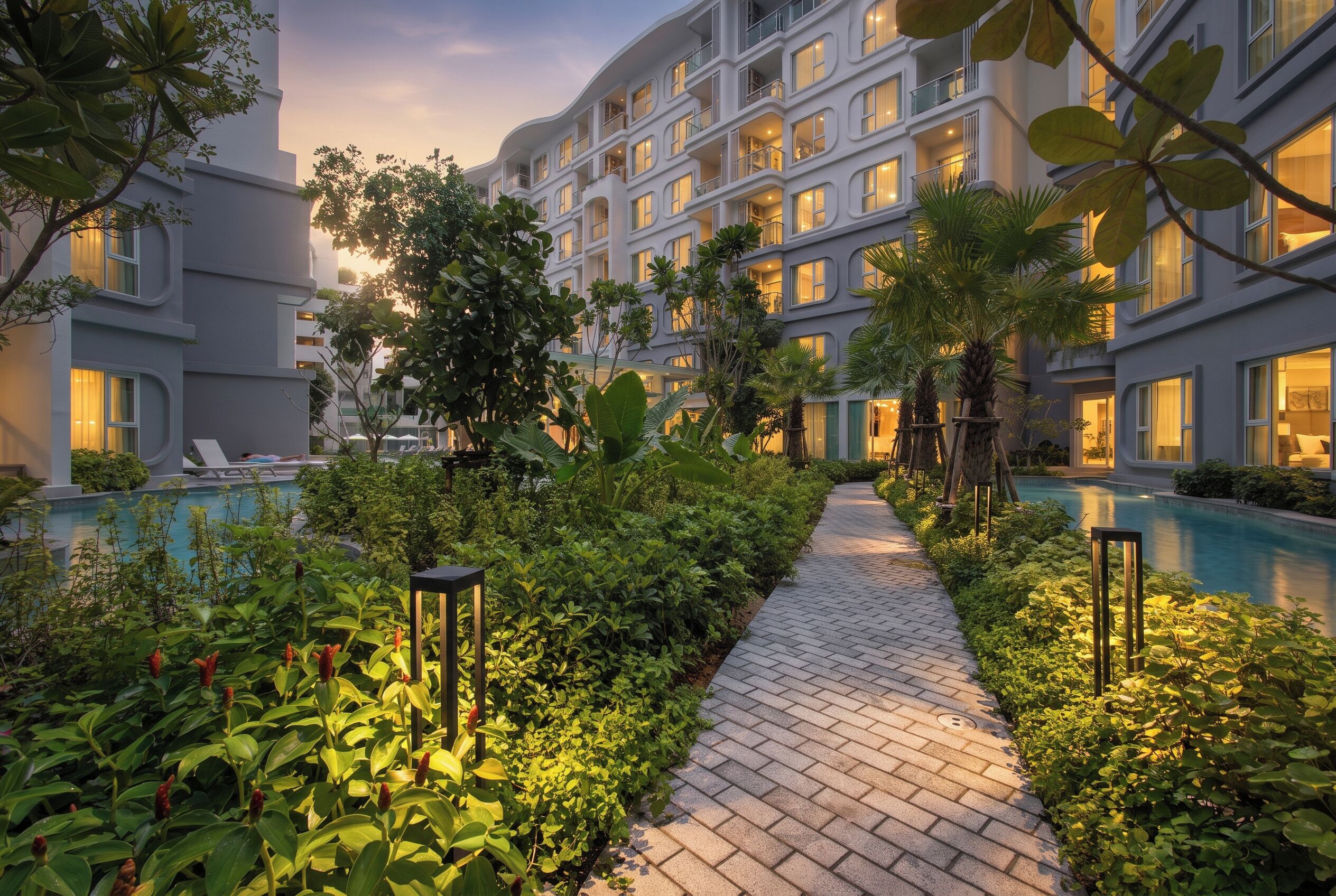 A hotel courtyard with a swimming pool, lush greenery, and a paved walkway.