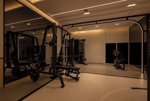 A modern gym with mirrored walls, weightlifting equipment, and a cardio machine. - Cozy 1-bedroom apartment in Title Serenity Naiyang (Thalang District)