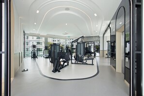 A modern gym with various exercise equipment, a curved ceiling design, and large windows offering views of buildings outside. - Cozy 1-bedroom apartment in Title Serenity Naiyang (Thalang District)