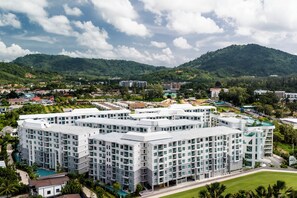 A multi-story hotel with a modern architectural design, featuring a central courtyard and a swimming pool. - Cozy 1-bedroom apartment in Title Serenity Naiyang (Thalang District)
