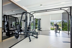 Ein modernes Fitnessstudio mit verschiedenen Trainingsgeräten, großen Fenstern und Blick ins Freie.