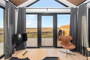A modern room with a large sliding glass door leading to an outdoor deck. - Arctic Exclusive Ranch (Kirkjubaejarklaustur)