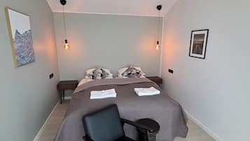 Un dormitorio moderno con una cama, dos mesitas de noche, una silla y una lámpara colgante.