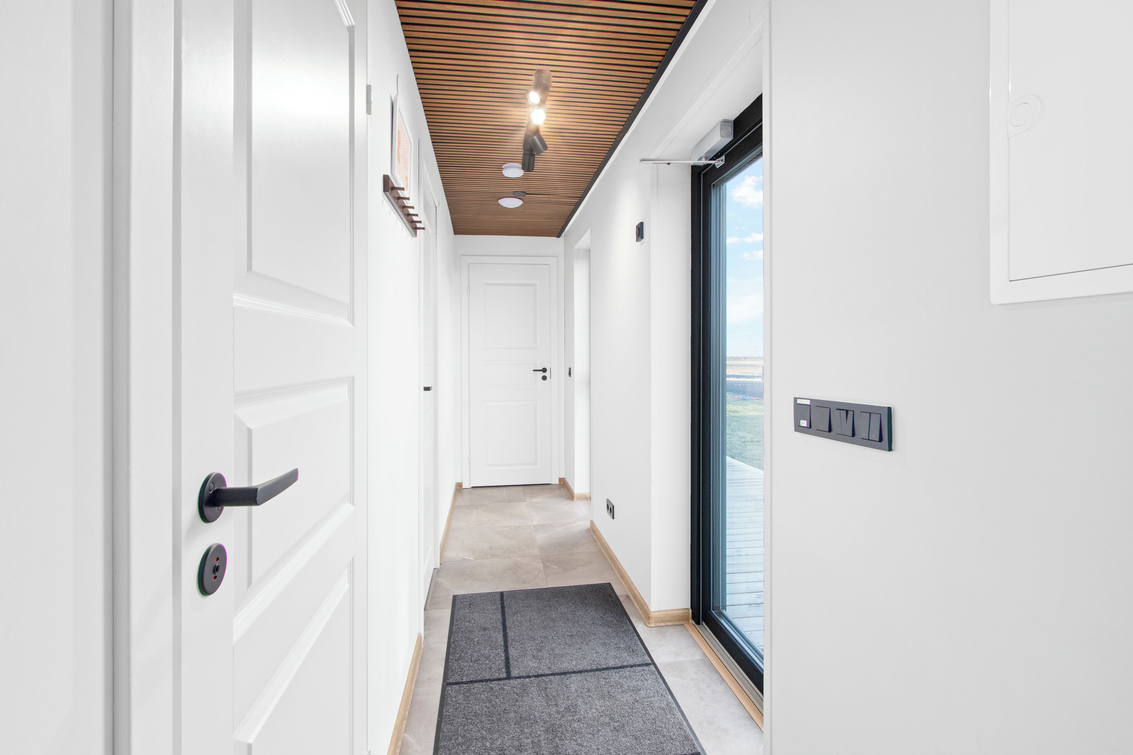 A modern hallway with white doors, a wooden ceiling, and a view through a glass door.