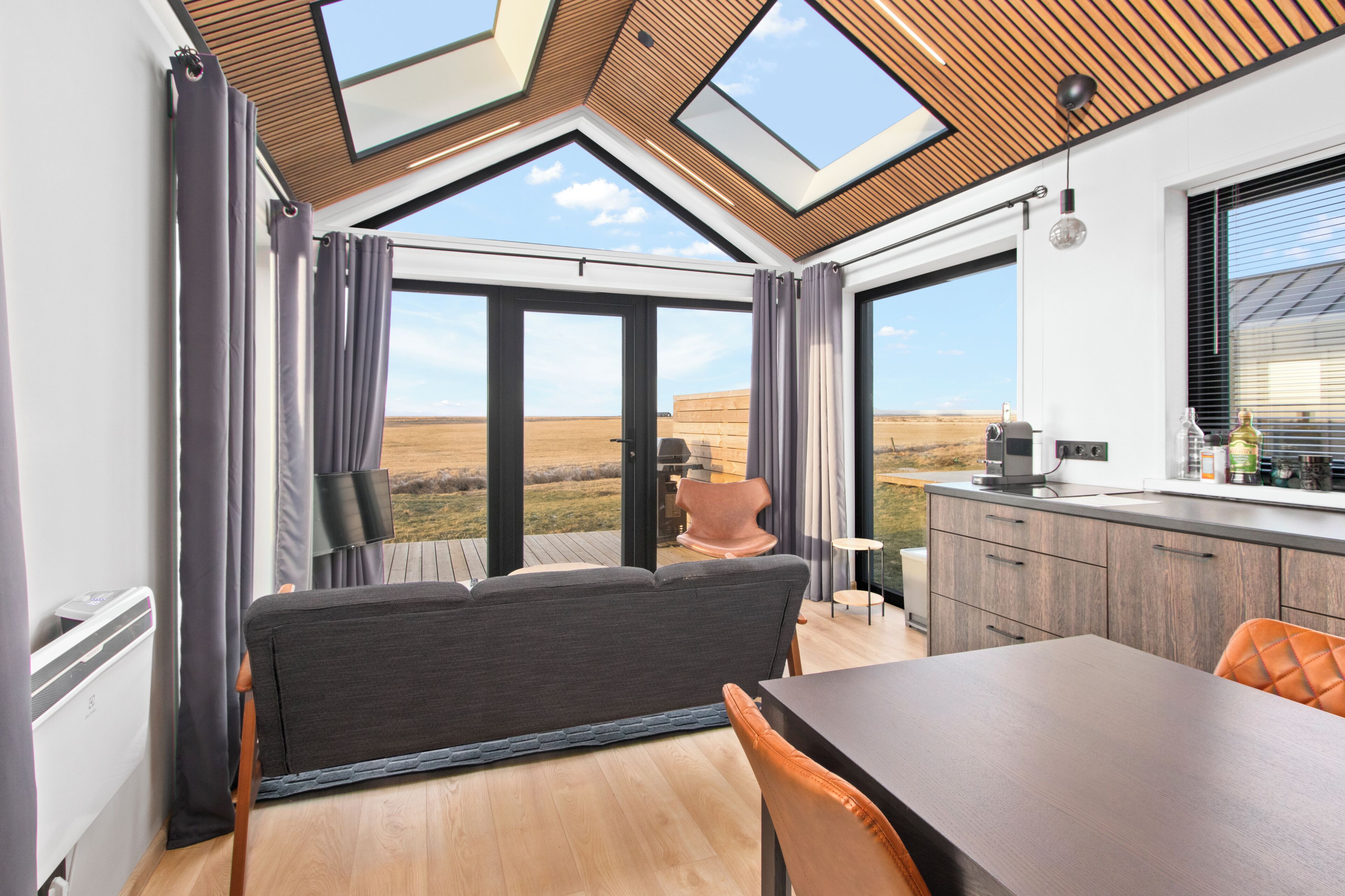 A modern interior with a dining area, a sofa, and a view of the outdoors.