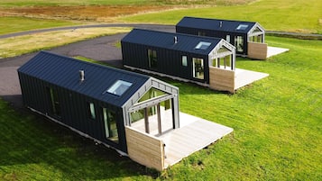 Tres cabañas modernas de color oscuro con grandes ventanales y terrazas de madera, ubicadas en un campo cubierto de hierba.