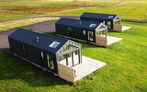 Three modern, dark-colored cabins with large windows and wooden decks, situated in a grassy field.