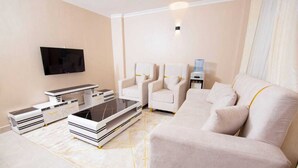 A modern living room with a flat-screen TV, a sofa, two armchairs, a coffee table, and a side table with a water dispenser.