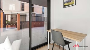 A modern room with a glass door leading to a balcony, a wooden desk, and a chair. - Metawisebnb Stylish 2BR Apartment Near Metro Shops (Sydney)