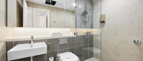 Et moderne badeværelse med en glasbrusekabine, en hvid vask og et toilet.